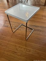 White square TV table with glossy top and chrome tubular legs on wooden floor