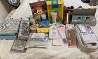 Photo showing an assortment of bath and beauty products including boxed soaps, manicure kit, lotions, foot care items, and shower curtain hooks laid out on a bed.