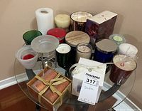 Full view of the assortment of candles on a small round glass table including pillar candles, votive candles, boxed sets, and various holders.