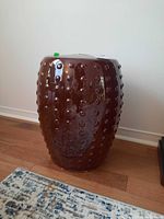 Brown ceramic stool with raised dots from side angle on wood floor next to rug