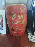 Full side view of red ceramic stool with yellow floral and bird designs, showing embossed circle pattern.