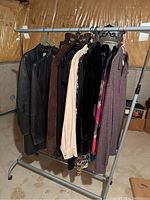 Wide view of rack holding seven pieces of ladies clothing including leather jackets, sweaters, and tops in dark and neutral colors.