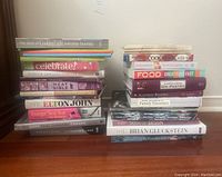 Photo of two stacks of assorted cookbooks and one autobiography book on a wooden floor against a plain wall. Titles visible include cookbooks and 'A Promised Land' by Barack Obama.