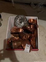 Box containing multiple copper molds, a small copper jug with handle, copper sauté dish, and a silver mold.