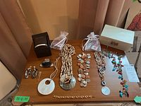 Full view of costume jewelry lot displayed on wooden table including necklaces, bracelets, earrings, brooches, and jewelry box