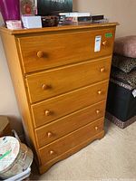 Front and slightly angled view of the medium-tone wood dresser showing five drawers with round wood pulls, some finish wear and scratches visible on the drawer fronts and edges.