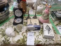 Photo showing Nova Scotian crystal desk clock, ceramic music box, salt shakers including Villeroy and Boch hedgehog, Eiffel Tower set, wooden matches, and other small items on table.