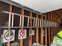 Full length view of 12 foot aluminum extension ladder mounted horizontally on garage wall, showing rubber feet at bottom end and structural frame.
