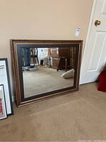 Mirror leaning against a wall on carpet. Shows framed bevelled edges with gold painted accents.
