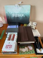 Photo showing a variety of notebooks including a leather bound journal, Moleskine notebooks, and two pen sets in packaging.
