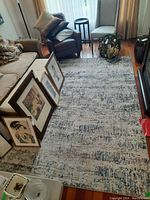 Rectangular machine made area rug spread on wood floor with living room furniture around. Rug has a distressed pattern with cream, gray and charcoal colors.
