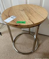 Perspective view of round side table with visible wood grain top, metallic supporting legs, and base ring.