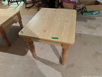 Light natural wood side table with turned, carved legs on a basement floor, showing the front and top views.