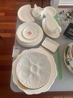 Overview of porcelain and ceramic dishes laid out on table showing crescent moon-shaped dishes, round plates, rectangular dish, gravy boat and teapot.