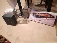 Photo of set showing black-boxed wine glasses, clear jar with funnel top, and boxed double burner griddle.