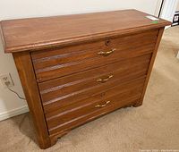 Front view of wood dresser showing three drawers with brass-tone handles and keyholes.