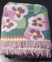 Folded view of blanket showing pansy floral pattern and fringed edge in pink, yellow, and green colors.