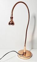 Full view of the copper tone desk lamp showing flexible neck, weighted round base with power cord, and flared lamp head.