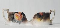 Front view of hand-painted Noritake porcelain spoon holder showing elongated shape with two handles and rose floral decoration.