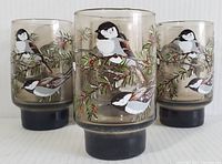 Four vintage Libbey brand footed beverage glasses with bird and branch design, shown grouped together.