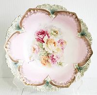 Front view of antique RS Prussia bowl showing scalloped shape, pink background, hand-painted rose bouquet center, and gilded accents.