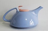 Side profile of teapot showing powder blue body with pink lid and handle, geometric handle shape, glossy finish.