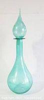 Front view of light turquoise blown glass genie bottle with rounded base and tall narrow neck, topped with elongated stopper.