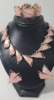 Complete set with necklace on display bust, matching bracelet behind, and earrings below. Shows geometric Art Deco style elements in pink with gold-tone metal.