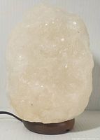 Front view of natural white Himalayan salt lamp glowing on wooden base