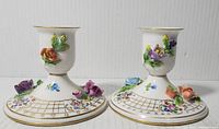 Pair of antique Dresden porcelain candle holders with hand-painted 3D floral appliques and gold accents photographed side by side on neutral background.