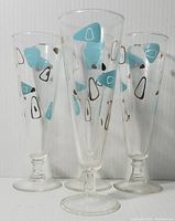 Front and angled view of four 1950's Federal Glass Atomic Amoeba/Boomerang pilsner glasses showing their shape, color pattern and size.