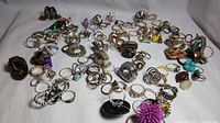 Wide view of multiple vintage fashion rings of various styles, sizes, and materials spread out on a white background.
