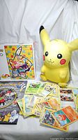 Photo showing Pikachu plush, loose Pokemon cards spread out, and the box for the 500-piece Pokemon puzzle with Pikachu image on it