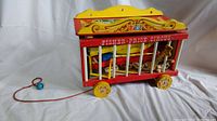 Wooden red and yellow Fisher Price circus cage train car containing wooden circus animals, shown from the front side with pull string and blue wooden ball at end.