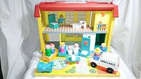 Front view of the Children's Hospital playset open with six figures arranged, ambulance vehicle, two hospital beds, and additional accessories inside the two-story plastic playhouse.