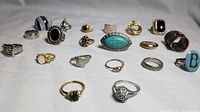Multiple rings arranged in two rows showing variety of stones and metal finishes including turquoise, clear crystals, and colored stones.