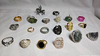 Photo showing full lot of 20 assorted fashion rings with mixed metals and various stone settings, laid out on white background.
