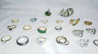 Photo showing 20 assorted fashion costume rings arranged on white surface displaying various styles and stones.