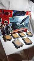 Photo of the Harry Potter Magical Beasts board game box with some visible wear, six stacks of Magic The Gathering cards arranged in front
