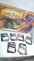 Photo showing Harry Potter Sorcerer's Stone board game box with multiple stacks of Magic The Gathering cards in front of it.