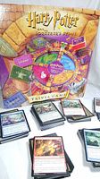 Photo showing Harry Potter Sorcerer's Stone Trivia Game box with game board and stacks of Magic The Gathering cards spread around.