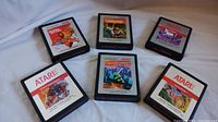 Photo showing all six Atari 2600 game cartridges laid out on a white fabric surface, identifiable titles include Crystal Castles, Jungle Hunt, Phoenix, Real Sports Football, Moon Patrol, and Centipede.