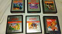 Top view of six Atari 2600 video game cartridges showing game titles and labels including Moon Patrol, Phoenix, Jungle Hunt, Crystal Castles, Centipede, and Real Sports Football.