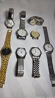 Eight vintage men's wristwatches laid out on white surface, showing variety in band types and dial colors.