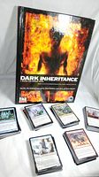 Dark Inheritance RPG campaign book with fiery silhouette on cover, surrounded by stacks of Magic The Gathering cards.