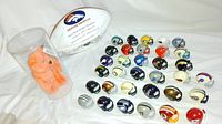 Photo showing limited edition Denver Broncos football signed by Mark Schlereth, John Elway Beanie Baby in case, and 33 miniature football helmets from various teams.