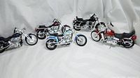 Five Maisto 1/12 scale Harley Davidson motorcycle models arranged on white background, showing various angles and colors including blue, red, black, and purple.