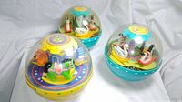 Three vintage Fisher Price Roly Poly Chime Balls: two green 1966 models with swan and butterfly figures inside domes, and one yellow 1985 carousel horse model.