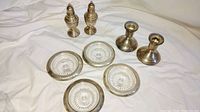 Photo showing 4 matching crystal ashtrays with silver rims, 2 weighted sterling silver candle stick holders, and 2 weighted sterling silver salt and pepper shakers grouped together on a white cloth background.