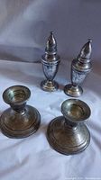 View of the vintage sterling silver salt and pepper shakers alongside two weighted sterling silver candle stick holders on a gray background showing intricate engraving and patina.